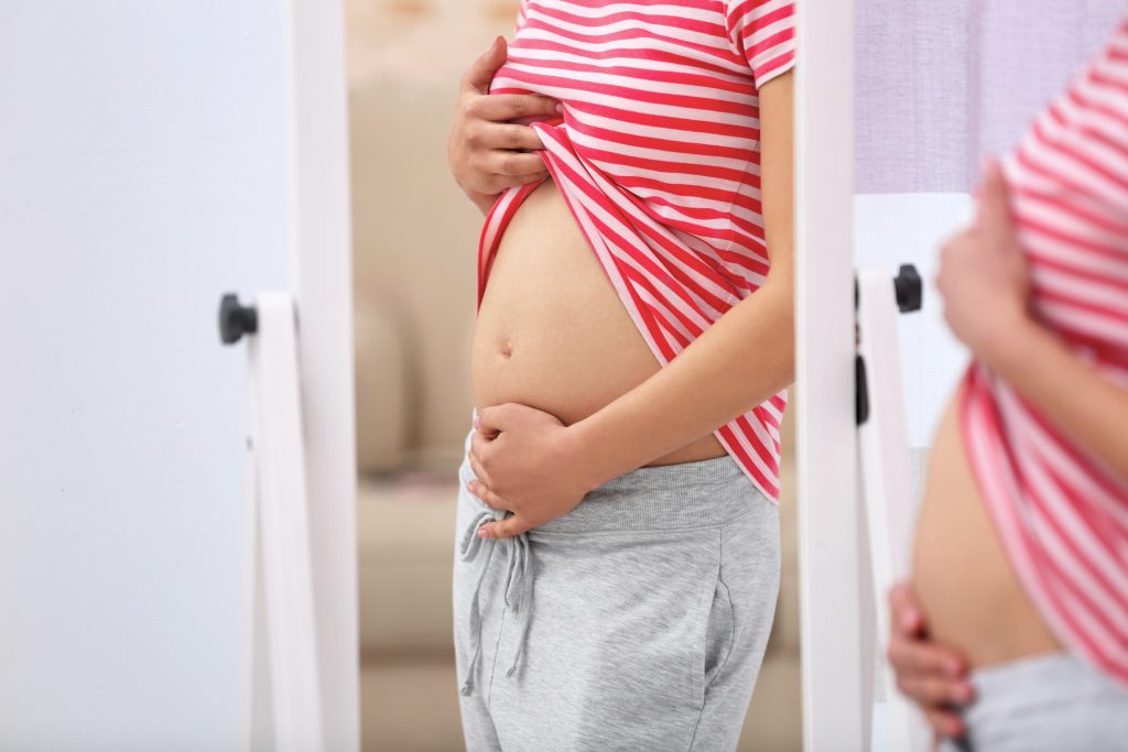 newly pregnant mom looking in mirror at first trimester growing belly.