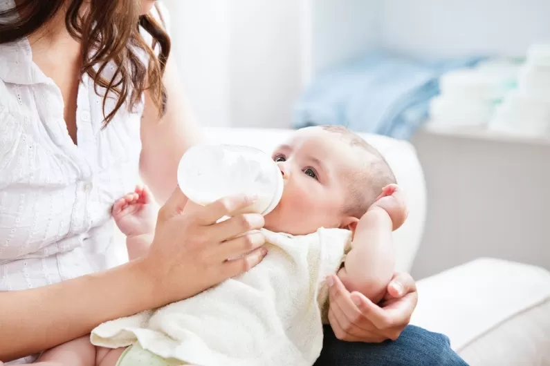 Bright mother formula feeding her son in the kitchen at home.