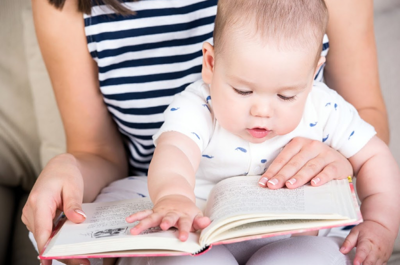 mom reading board book to one-year-old baby