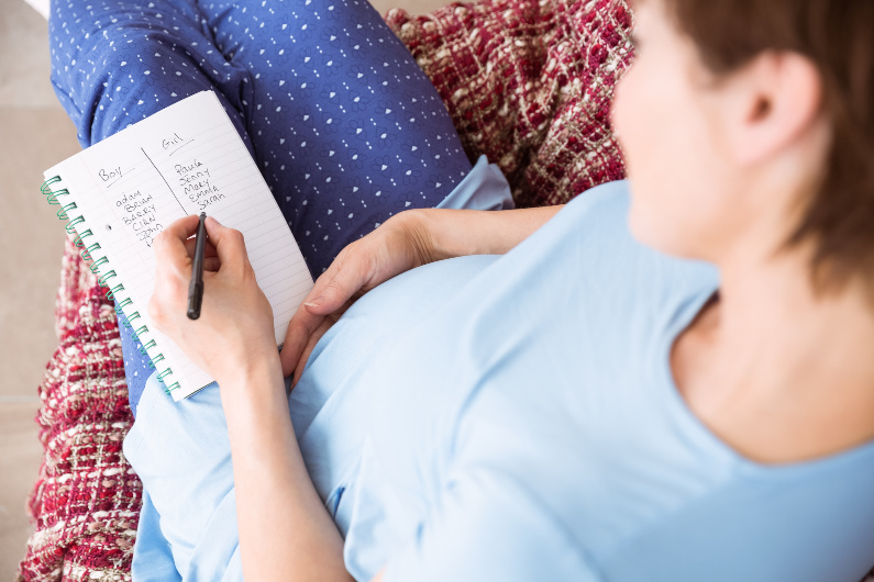 Pregnant Woman Writing Unique Baby Names on a Notepad