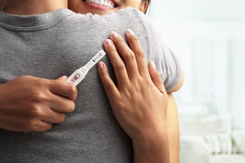 woman with positive pregnancy test smiling and hugging partner