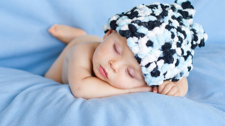 sleeping baby boy lying on blue blanket and fuzzy hat