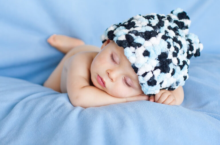 sleeping baby boy lying on blue blanket and fuzzy hat