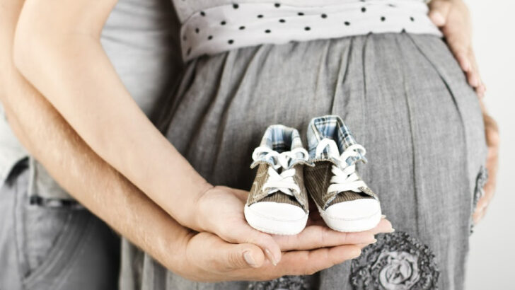 newly pregnant couple holding newborn baby shoes