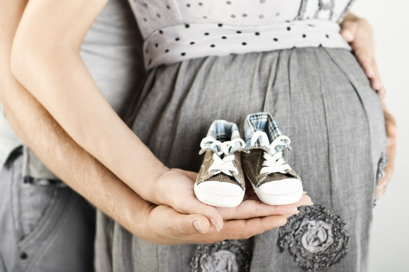 newly pregnant couple holding newborn baby shoes, reading to start their baby registry