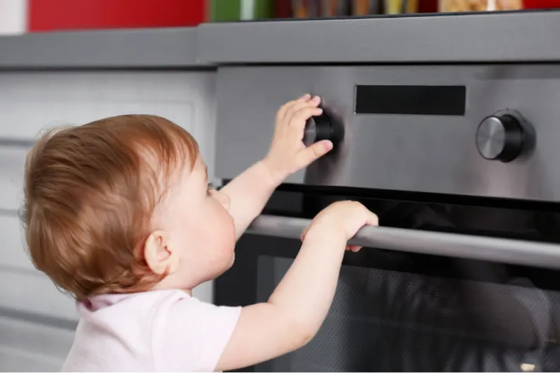 baby touching oven knob on stove