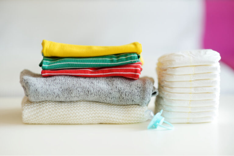 0-3 months baby clothes folded and stacked neatly, next to stack of diapers.
