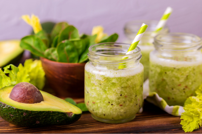 folate-rich avocado smoothie in mason jar with straw, next to halved avocado on table.