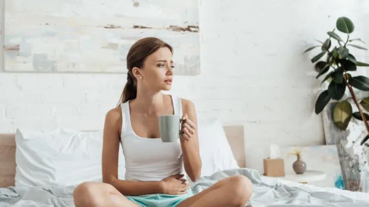 woman going through a miscarriage, sad sitting on bed with coffee mug
