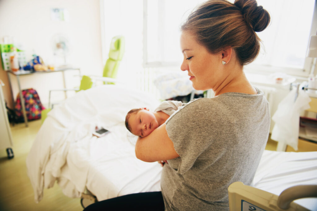 new mom a few hours postpartum, holding newborn in hospital room