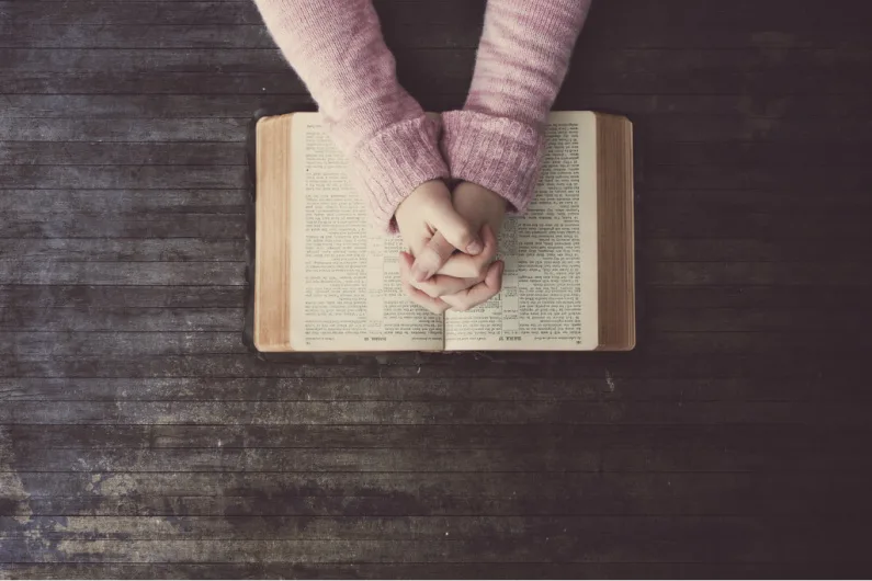 Woman praying over a Bible on a wooden table.