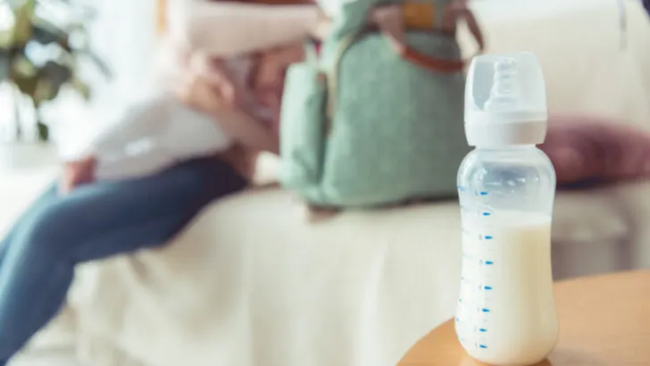 formula feeding mom holding baby with bottle of formula on table