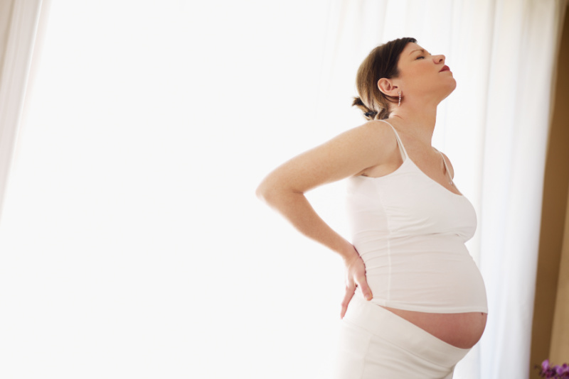 pregnant woman struggling with back pain, holding her back with eyes closed.