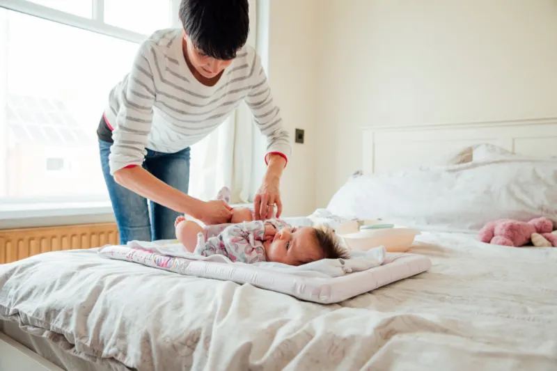mom bending over bed to change baby's diaper