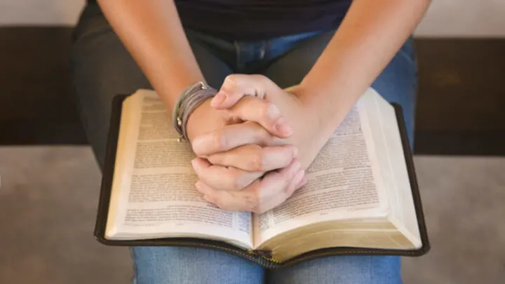 wife praying scriptures over her husband, folding hands on Bible