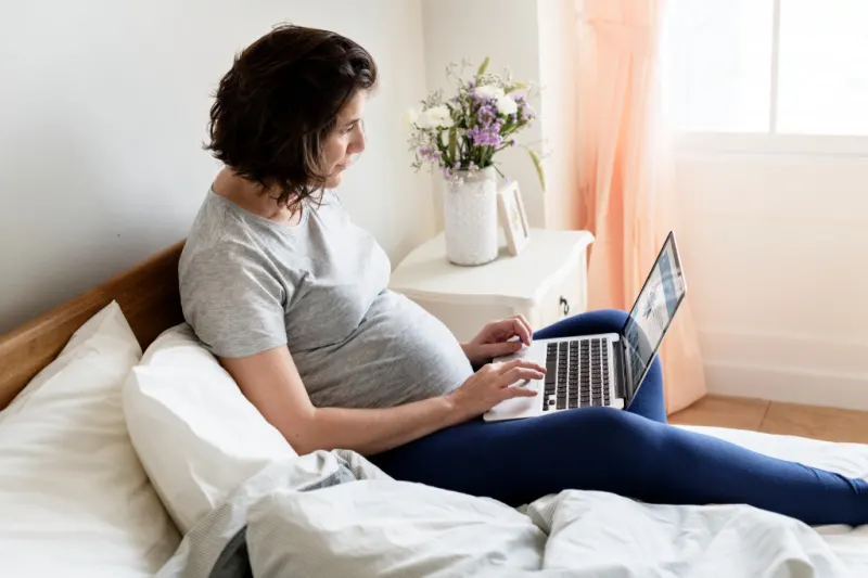 pregnant woman reading baby registry tips on laptop in bed