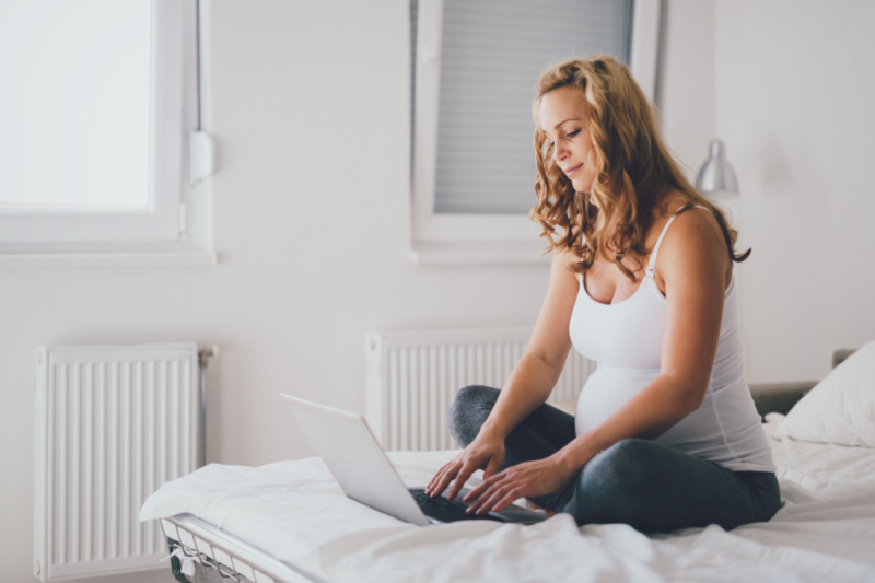 pregnant woman sitting on a bed with a laptop adding items to her baby registry