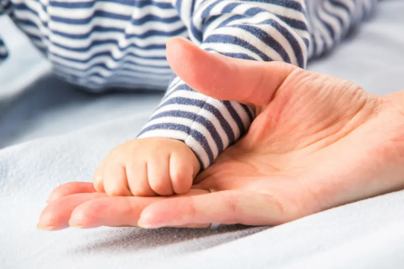 close up of mom's hand holding newborn baby's hand in hospital bed after successful natural birth