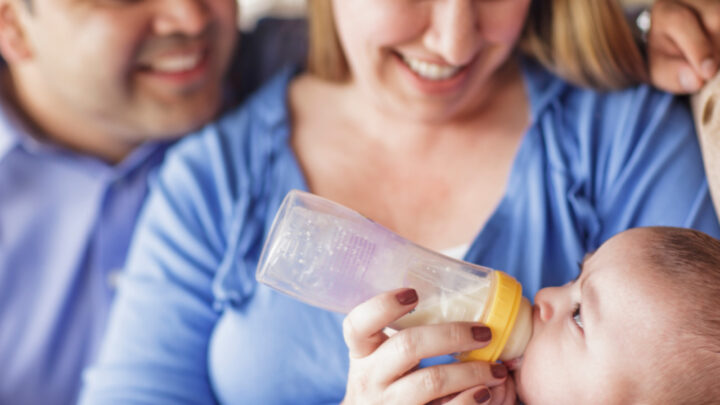 parents holding baby while bottle feeding with formula