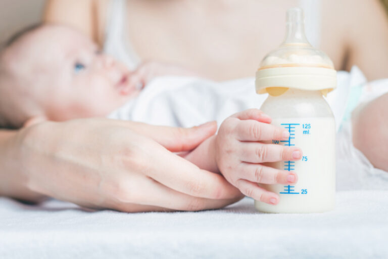 baby holding bottle with one hand while being held by mother