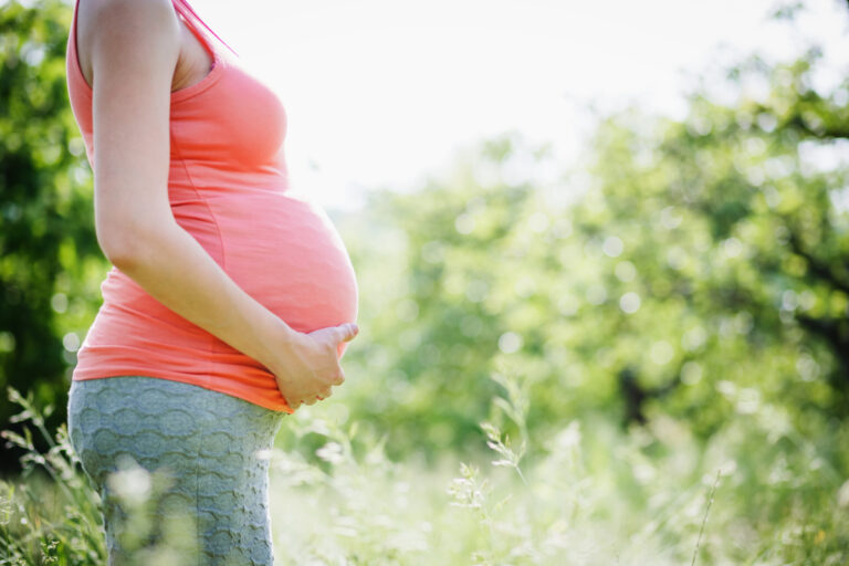 side view of pregnant woman's belly, side view in long pink tank top holding belly