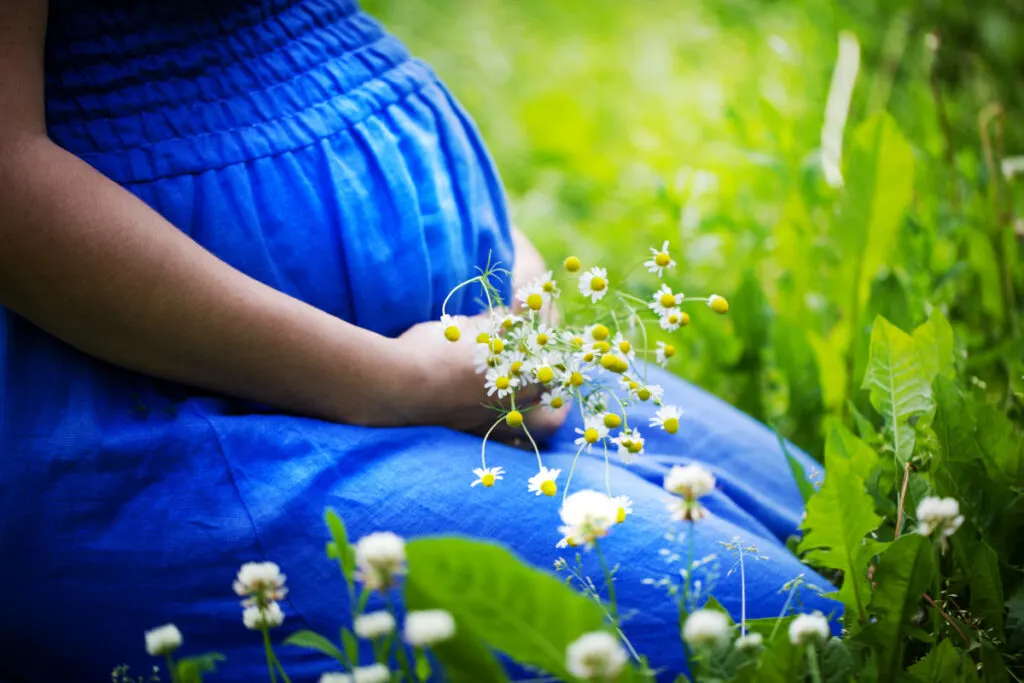 pregnant woman sitting in a field with flowers in her hand, considering plant names for boys