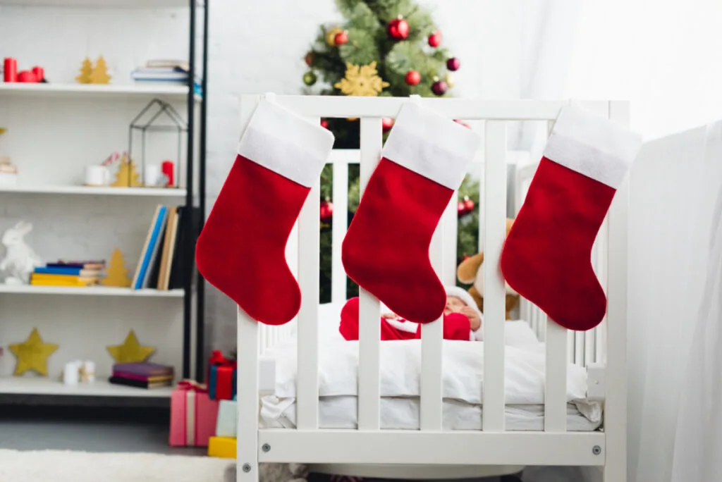 Christmas stockings hanging on newborn crib, baby's first Christmas theme with Christmas tree in background