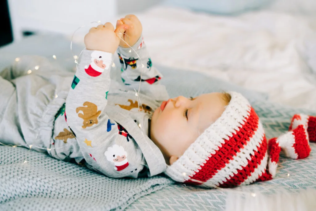 newborn baby lying on back dressed for christmas playing with christmas lights