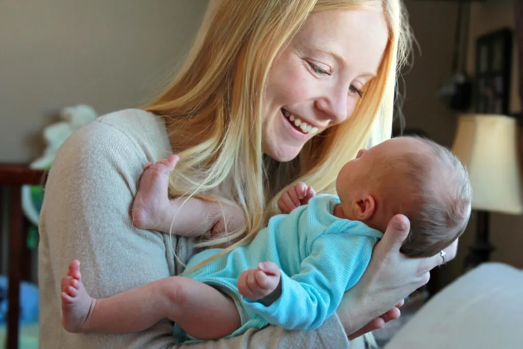 blond white new mom holding newborn baby in arms and smiling