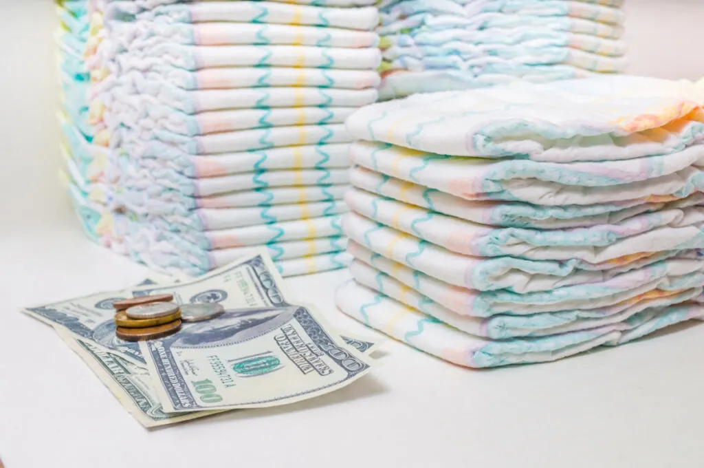 stacks on diapers next to hundred dollar bill and coins, diapers are expensive concept