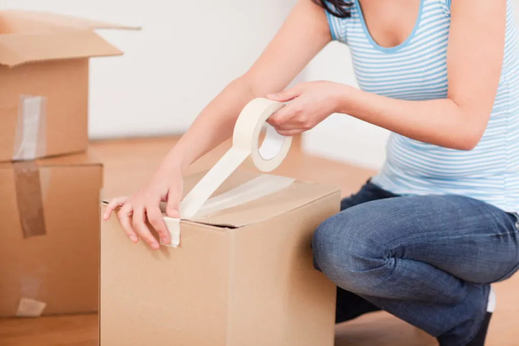 woman packing baby stuff into brown cardboard box 