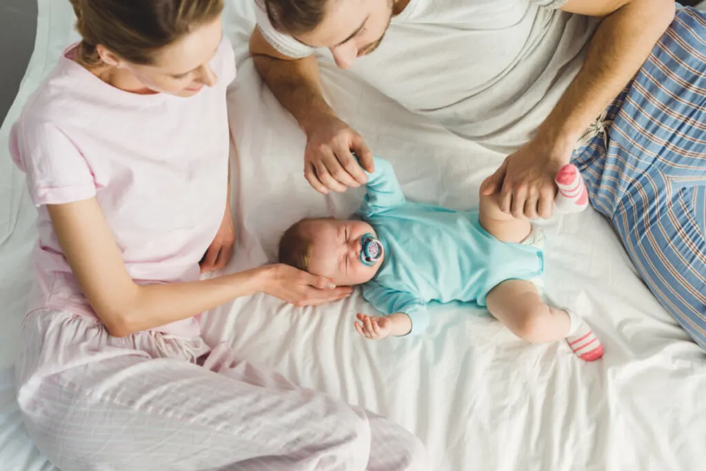 mom and dad laying with newborn on bed, comforting crying baby together