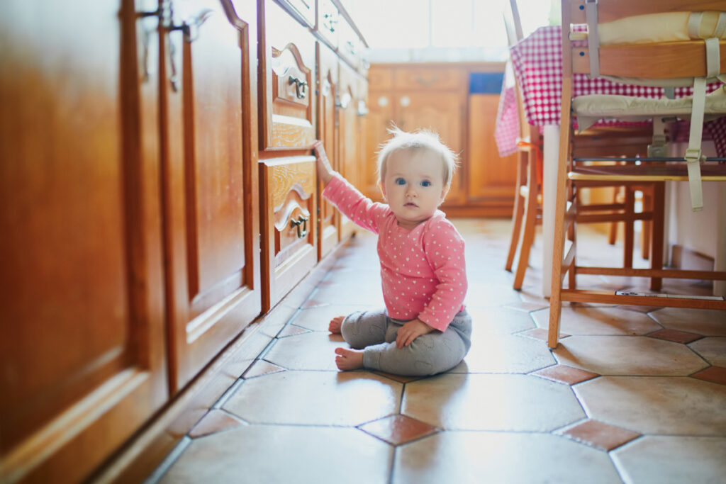 9 month old baby sitting on kitchen floor pulling at cabinets