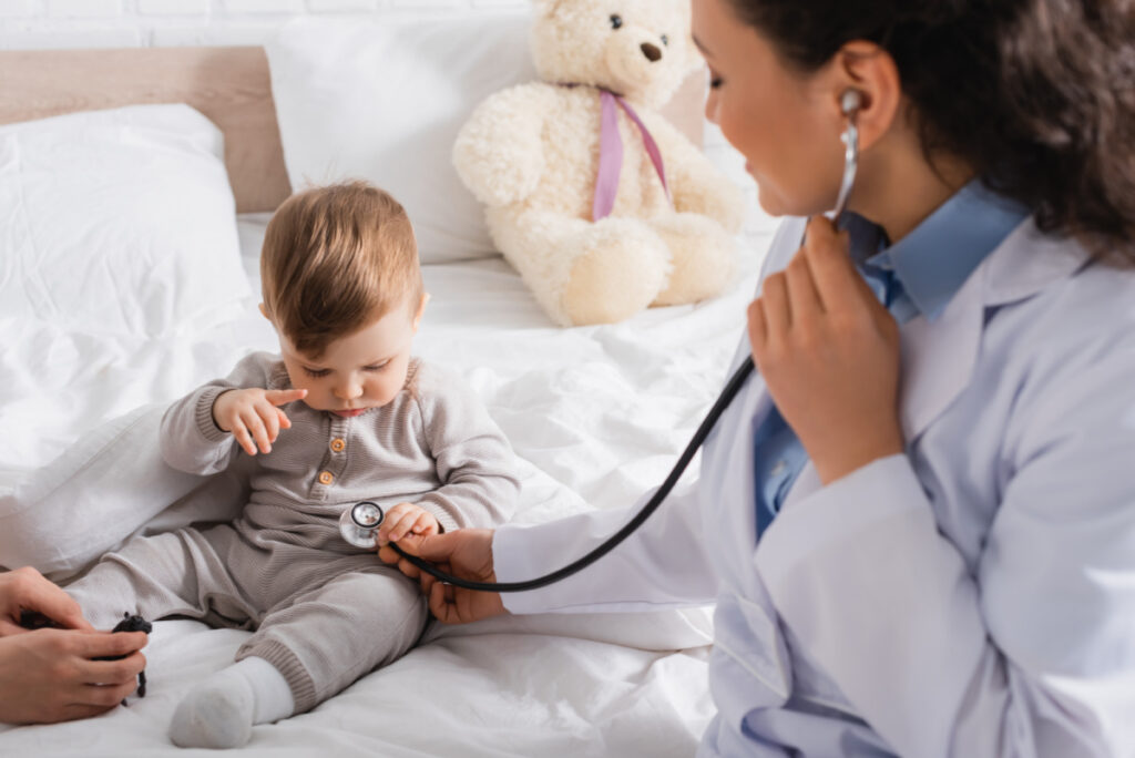 pediatrician using stethoscope to check young baby's belly sounds