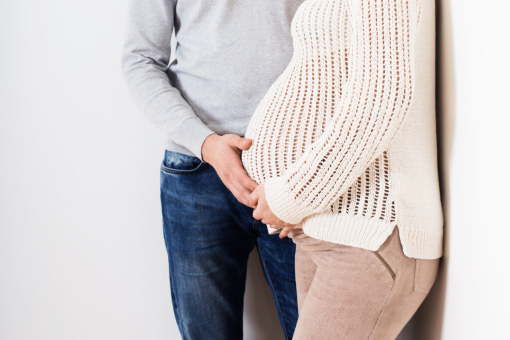 pregnant couple standing together, dad's hand on mom's belly