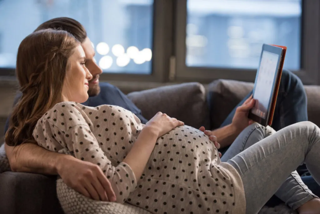 husband and pregnant wife discussing parenting styles while laying on couch together