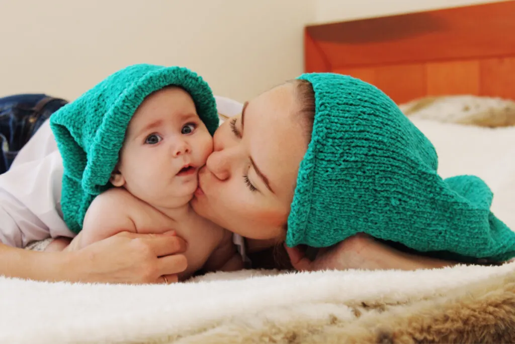 mother lying on bed kissing her 6 month old baby