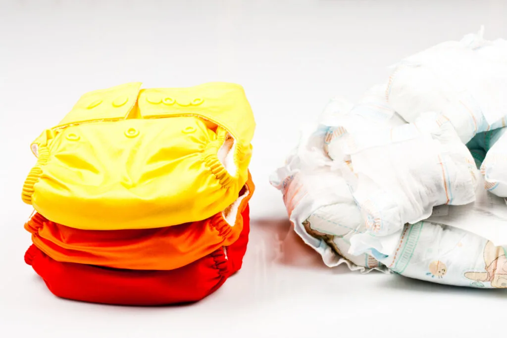 stack of reusable cloth diapers next to pile of used disposable diapers