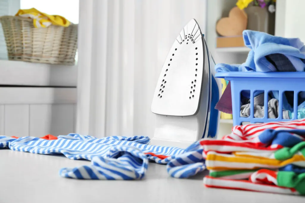 baby clothes folded and laying on table next to iron