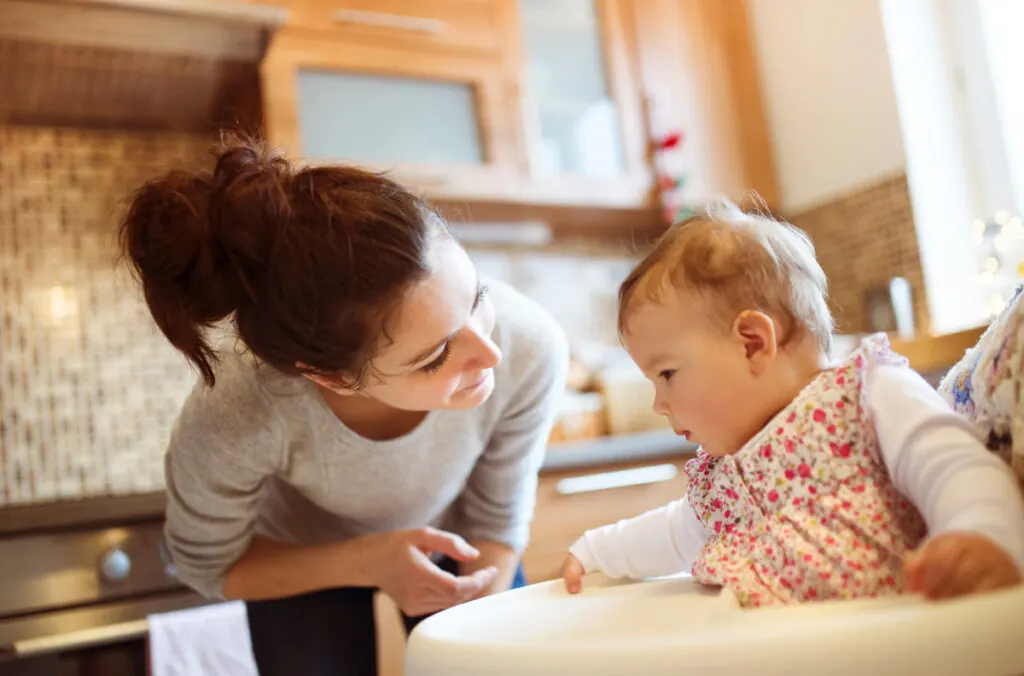 busy mom smiling and talking to clingy baby in high chair