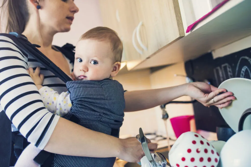 mom wearing baby in carrier doing dishes