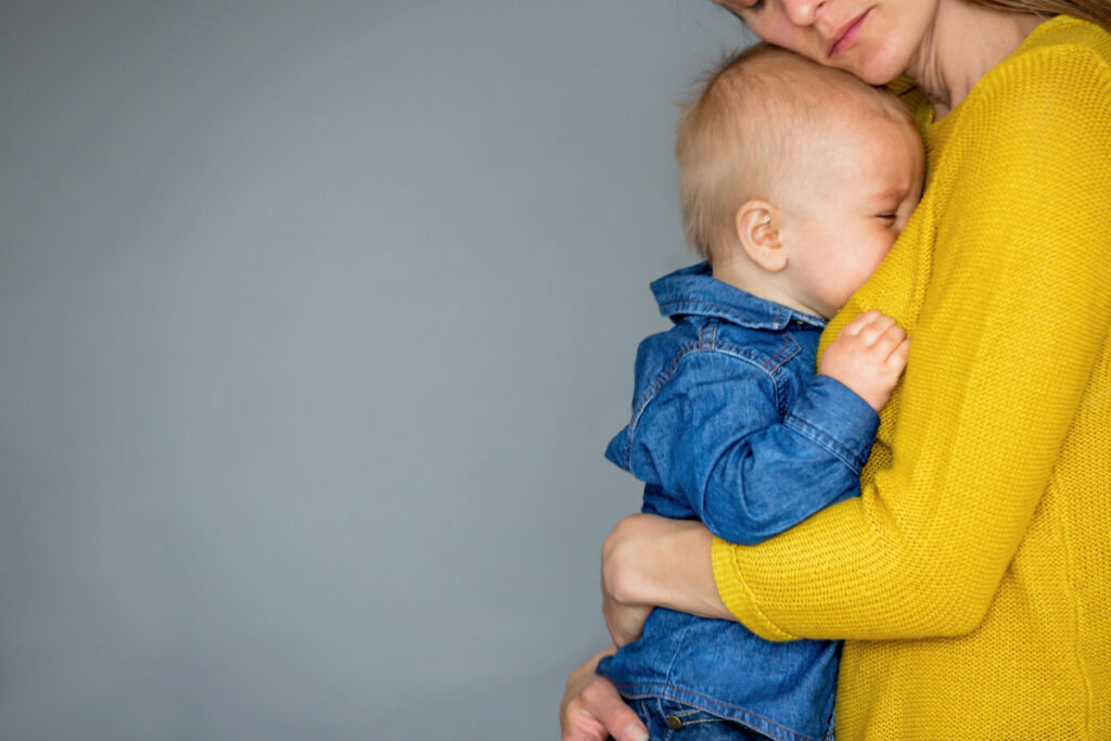 mom in yellow sweater comforting older, crying baby