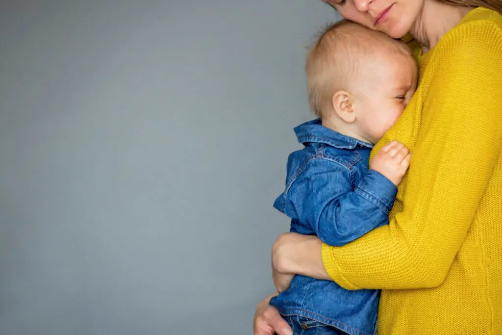 mom in yellow sweater comforting older, crying baby