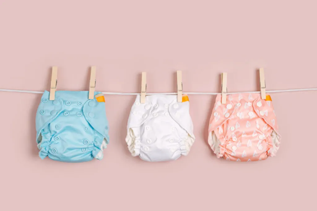 Reusable cloth baby diapers drying on a clothes line on pink background.