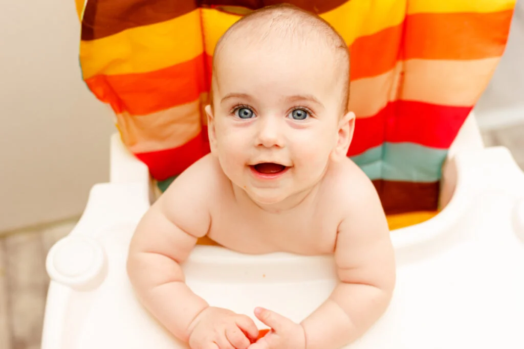6 month old sitting in colorful high chair looking at camera