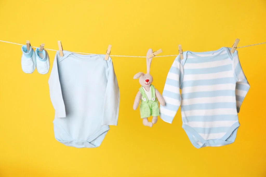 two long sleeve baby onesies, booties and stuffed animal hanging from clothes line, on yellow background