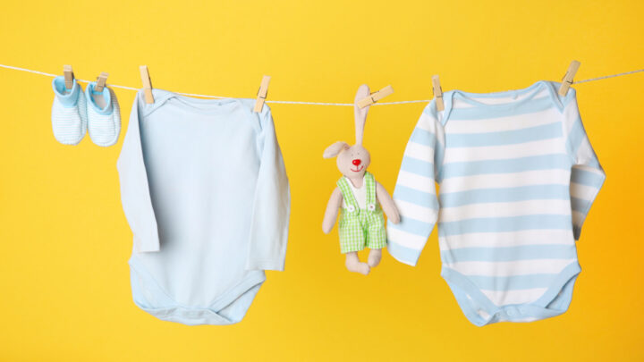 two long sleeve baby onesies, booties and stuffed animal hanging from clothes line, on yellow background