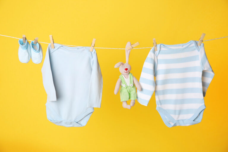 two long sleeve baby onesies, booties and stuffed animal hanging from clothes line, on yellow background