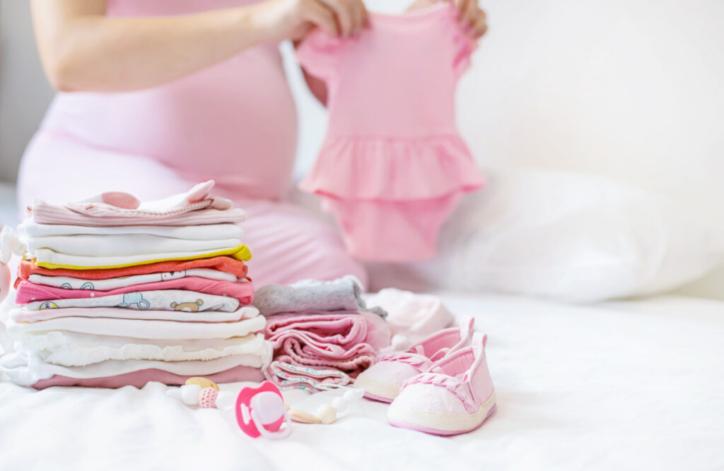 pregnant mom folding baby clothes and creating capsule wardrobe for newborn