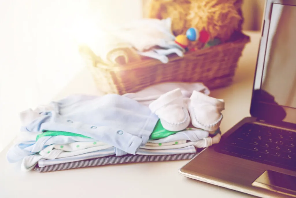 baby capsule wardrobe pieces folding neatly on counter next to laptop